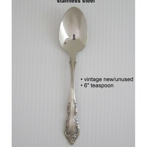 May include: A silver teaspoon with an ornate handle. The spoon is 6 inches long and is vintage but new and unused.