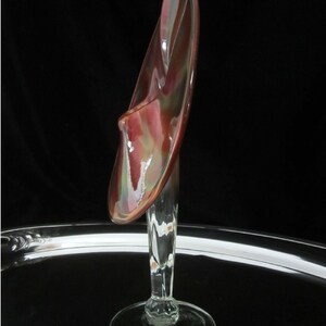 May include: A glass vase with a unique, abstract design. The vase is made of clear glass with a red, brown, and green iridescent finish. The vase has a tall, slender stem and a wide, open mouth.