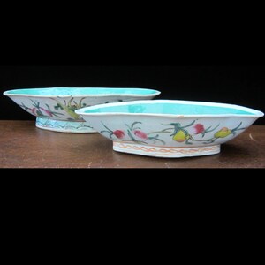 May include: Two white porcelain bowls with a turquoise glaze and floral designs. The bowls are oval shaped and have a raised rim.