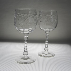 May include: Two clear glass wine glasses with intricate etched designs. The glasses have a tall, slender stem and a round bowl.