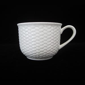 May include: A white ceramic coffee cup with a woven basket pattern. The cup has a rounded body, a curved handle, and sits on a black background. The cup is made of ceramic and is suitable for hot beverages.