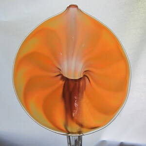 May include: A glass vase in the shape of a flower with a swirling orange and white design. The vase is clear glass with a brown stem.
