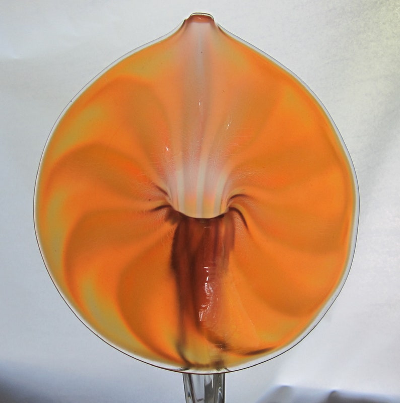 May include: A glass vase in the shape of a flower with a swirling orange and white design. The vase is clear glass with a brown stem.