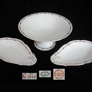 May include: A set of three white porcelain serving dishes with a brown and gold floral design. The dishes are in the shape of a bowl and two oval plates.