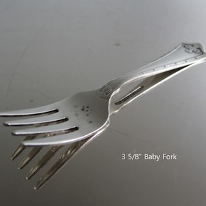 May include: A silver baby fork with a 3 5/8" length. The fork has a decorative design on the handle.