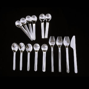 May include: A collection of shiny, silver-colored cutlery, including spoons, forks, and a knife, arranged against a stark black background. The spoons have rounded bowls and long, slender handles. The forks have four tines, and the knife has a simple, elegant design.