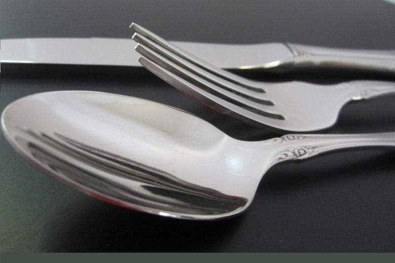 May include: A set of silverware with a spoon, fork, and knife. The silverware is made of polished stainless steel and has a traditional design.