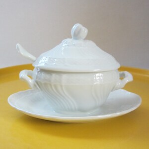 May include: White porcelain gravy boat with a lid and a matching saucer. The gravy boat has a fluted design and a small handle on each side. The lid has a decorative knob.