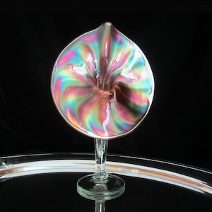 May include: A iridescent glass vase with a swirl pattern in shades of pink, blue, and green. The vase has a trumpet-shaped opening and a clear glass stem.