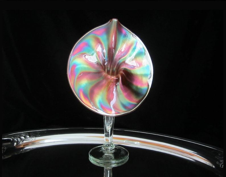 May include: A iridescent glass vase with a swirl pattern in shades of pink, blue, and green. The vase has a trumpet-shaped opening and a clear glass stem.