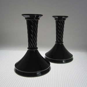 May include: A pair of black glass candle holders with a twisted design. The holders have a wide base and a narrow neck.