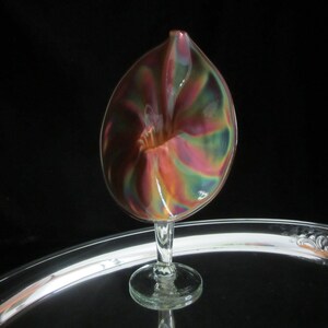 May include: A iridescent glass vase with a unique swirl design. The vase is shaped like a flower and has a clear glass stem.
