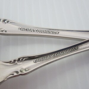 May include: Close-up of the back of two silver spoons with the words "Oneida Community" engraved on the handles.