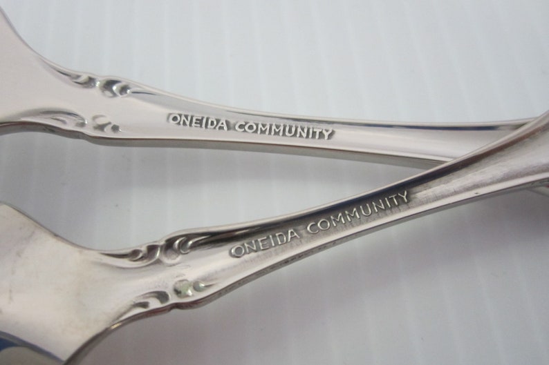 May include: Close-up of the back of two silver spoons with the words "Oneida Community" engraved on the handles.