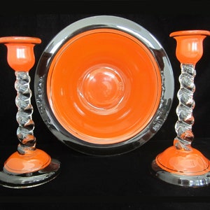 May include: A set of three orange and black ceramic candle holders. The candle holders have a twisted glass stem and a wide base.