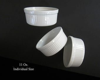 May include: Three white, individual-sized ramekins with vertical ribbed detailing. The ramekins are 11 oz. each and are displayed against a dark background. The text "11 Oz. Individual Size" is visible.