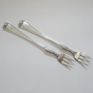 May include: Two silver cake forks with ornate handles. The forks have three tines each.