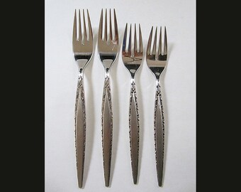 May include: A set of four silver-toned metal forks arranged vertically. Each fork features a polished four-tine head and a tapered handle with a textured, decorative border along the edges and a smooth, matte-finished center panel.