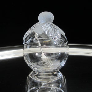 May include: A clear glass sugar bowl with a frosted lid shaped like a stylized fruit. The bowl has a decorative design and a small spoon inside.