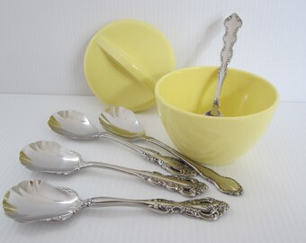 May include: A collection of vintage serving pieces. Includes a pale yellow bowl and lid, four silver serving spoons with shell-shaped bowls, and a small silver spoon inside the bowl. The spoons have ornate handles.