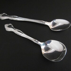 May include: Two silver spoons with ornate handles. The spoons are on a black background.