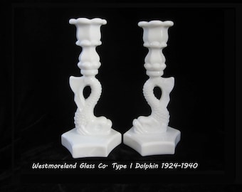 May include: Pair of white milk glass candle holders shaped like dolphins. The candle holders are in the style of Westmoreland Glass Company's Type I Dolphin pattern, which was produced from 1924 to 1940.