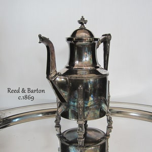 May include: Silver teapot with a round body and a decorative handle. The teapot has a lid with a finial and sits on four legs. The teapot is on a silver tray. Reed & Barton c.1869