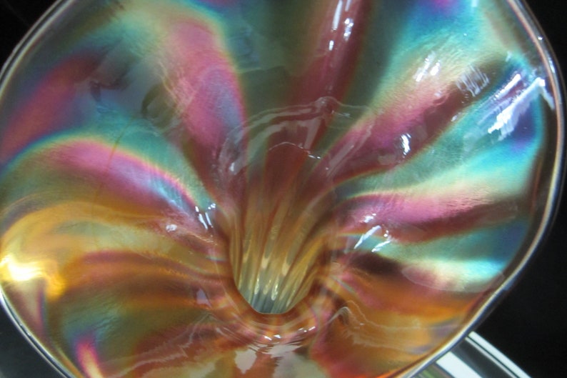 May include: A iridescent glass vase with a funnel-shaped opening. The vase has a swirling pattern of pink, blue, and green.