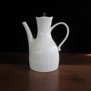 May include: White ceramic teapot with a ribbed design and a silver lid. The teapot has a spout and a handle.