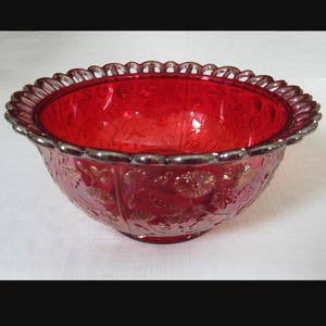 May include: A red glass bowl with a scalloped rim and a floral design. The bowl is made of ruby red glass and has a silver-colored rim.