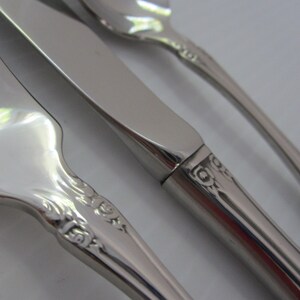 May include: Close-up of a set of silverware with ornate handles. The fork, knife, and spoon are made of polished stainless steel.