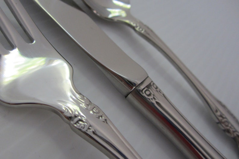 May include: Close-up of a set of silverware with ornate handles. The fork, knife, and spoon are made of polished stainless steel.