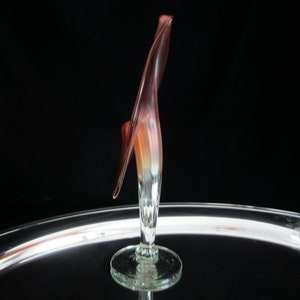May include: A glass sculpture of a flower with a long, thin stem and a single, large, red and orange petal. The sculpture is on a clear glass base.