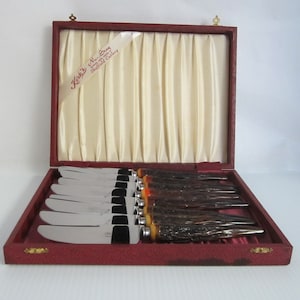 May include: A set of eight stainless steel butter knives with stag horn handles in a red velvet lined box. The box is labeled "Kirby & Sons Sheffield Cutlery".