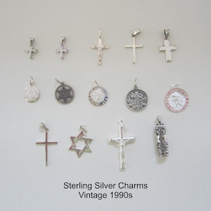 May include: A collection of vintage sterling silver charms from the 1990s. The charms include crosses, a Star of David, and religious medallions.