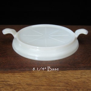 May include: White milk glass coaster with two handles. The coaster has a raised center with a starburst design. The base of the coaster is 8 1/4 inches in diameter.