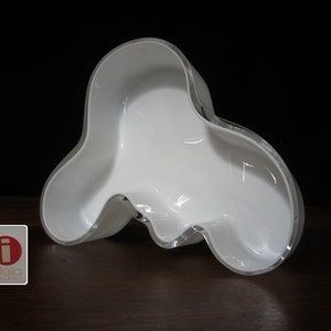 May include: White ceramic vase with an organic, asymmetrical shape. The vase has a smooth, glossy finish and a slightly translucent quality.