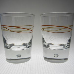 May include: Two clear glass shot glasses with a brown and yellow striped design and the word "Baileys" etched on the front.