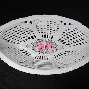 May include: White ceramic oval serving dish with a woven design and hand-painted floral accents in pink, yellow, and blue.