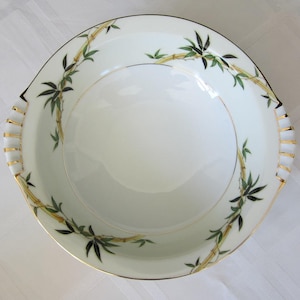May include: A white ceramic bowl with a gold rim and a green and gold bamboo design. The bowl is perfect for serving salads, fruit, or snacks.