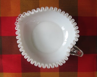 May include: White milk glass bowl with a scalloped edge and a silver handle. The bowl is on a red and brown checkered tablecloth.