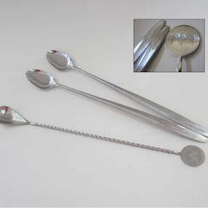 May include: Three silver cocktail spoons. Two spoons have a long, thin handle with a decorative floral design. The third spoon has a twisted handle and a round, decorative end.