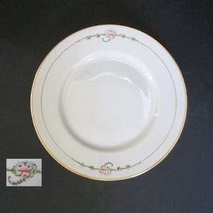 May include: White porcelain plate with a gold rim and delicate floral accents in pink, blue, and green. The plate has a simple, elegant design, suitable for serving meals. The plate is approximately 10 inches in diameter.