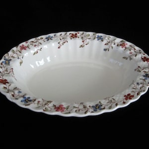 May include: White oval serving bowl with a floral pattern in shades of blue, red, and pink. The bowl has a scalloped edge and a slightly rippled surface.
