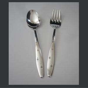 May include: A shiny silver spoon and fork set. The spoon has a rounded bowl, and the fork has four tines. Both utensils have long, slender handles with starburst designs. The set is likely for dining.
