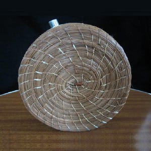 May include: A round, woven basket with a metal top. The basket is made of natural materials and has a brown and white colour scheme.