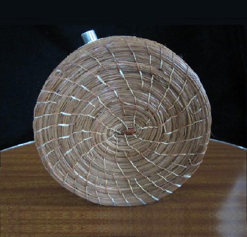 May include: A round, woven basket with a metal top. The basket is made of natural materials and has a brown and white colour scheme.