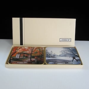 May include: Set of two square coasters with images of Japanese gardens. One coaster features a red and orange autumn scene with a pagoda and the text "TOJI-JI TEMPLE". The other coaster features a winter scene with snow-covered trees and the text "KEN-ROKUEN GARDEN".