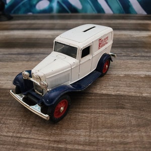 May include: A white and blue vintage toy truck with red wheels. The truck has the text "THE HOME SAVINGS & LOAN CO." on the side. The toy truck is a die-cast model.