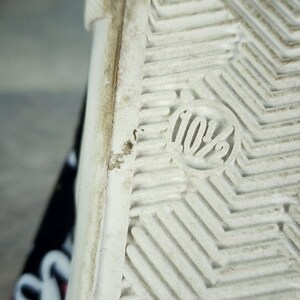 May include: The white rubber sole of a shoe features a textured herringbone tread pattern and a circular embossed marking displaying the size 10.5. The edge of the sole shows signs of wear, and a portion of the black patterned upper is visible.